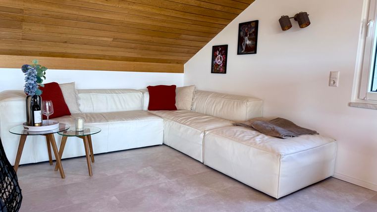 Een gezellige woonkamer met een witte L-vorm bank en rode kussens. Een bijzettafel van glas met twee glazen staat in het midden.
