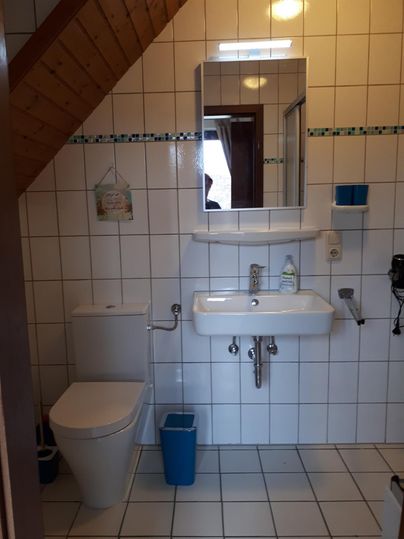 A simple bathroom with white tiles and a shower. There is a sink, a toilet, and a large mirror.