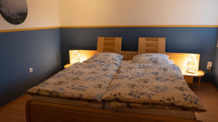 A cozy bedroom with a double bed and floral bedspreads. The walls are painted in blue and yellow, and there are bedside tables with lamps.
