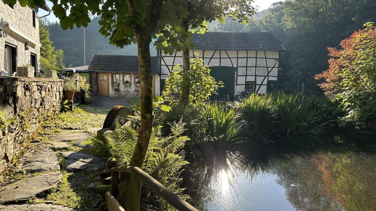 Een schilderachtige vijver omgeven door weelderig groen en bomen. Op de achtergrond is een traditioneel huis in vakwerkstijl te zien.