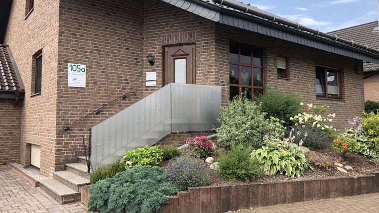 Ein modernes Einfamilienhaus mit einer Steintreppe und einem schönen Garten. Bunte Blumen und Sträucher schmücken den Eingangsbereich.