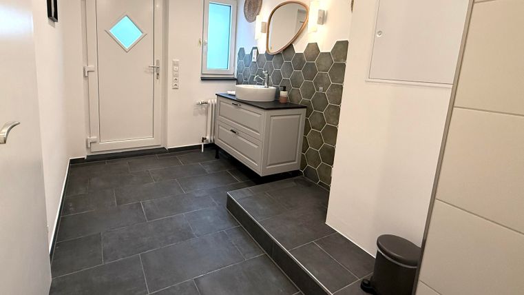 Een moderne hal met grijze tegels, een lichte entree en een stijlvolle wandbekleding van hexagonaal tegels. De ruimte is goed verlicht en mooi gedecoreerd.