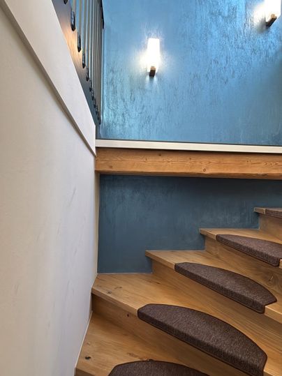 Een moderne trap van hout met gestoffeerde treden. De muren zijn in een stijlvolle blauwe kleur geschilderd en de verlichting zorgt voor een aangename sfeer.
