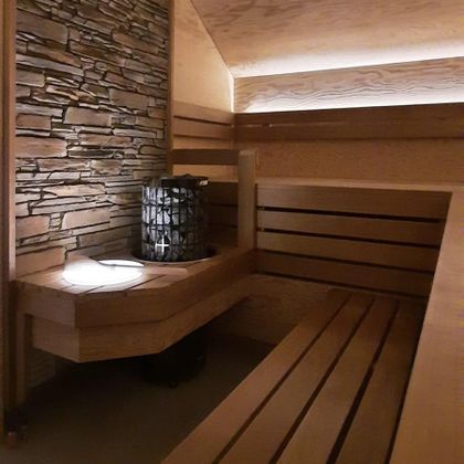A relaxing sauna room with wooden benches and a stone wall. Soft lighting creates a pleasant atmosphere.