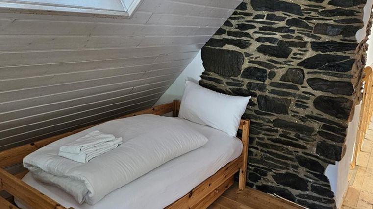 A cozy bedroom with a wooden bed and fresh towels. The walls are partially clad with natural stone, giving it a rustic charm.