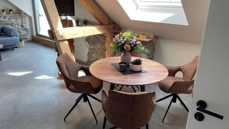 Een moderne eetkamer met een ronde houten tafel en bruine stoelen. Grote ramen zorgen voor veel daglicht en een uitnodigende sfeer.