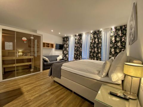 Ein modernes Hotelzimmer mit einem großen Bett, einem Sofa und stilvollen Vorhängen. Es gibt auch einen Tisch und einen Fernseher, was für Komfort sorgt.