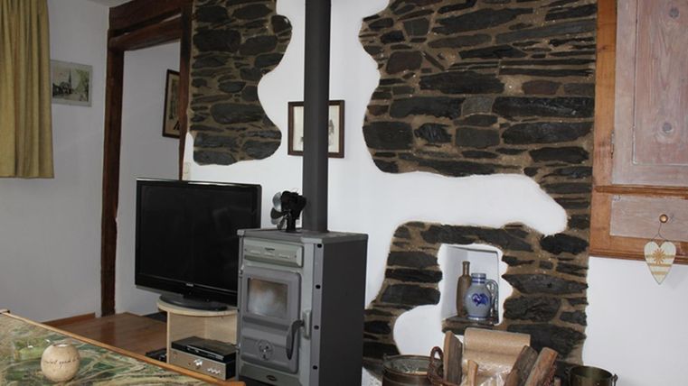 A cozy living space with a modern stove and a television. The walls are decorated with natural stones, which creates a rustic atmosphere.