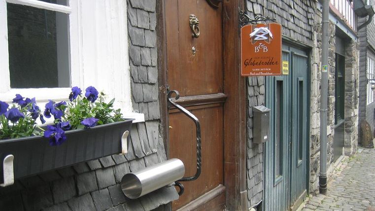 Ein charmantes Bed & Breakfast mit einer hölzernen Tür und einem einladenden Schild. Vor der Tür blühen violette Blumen in einem Blumenkasten.