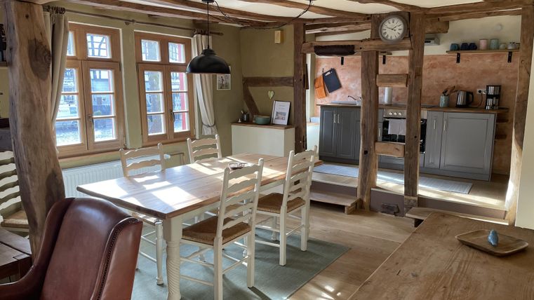 Een gezellige keuken met een grote eettafel en stoelen. Heldere ramen zorgen voor veel natuurlijk licht.