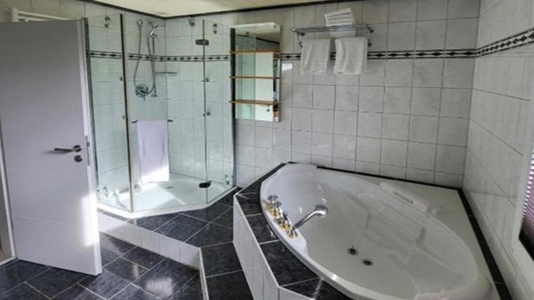 A modern bathroom with a bathtub and a separate shower. The walls are light-tiled, and there are towels in a practical holder.