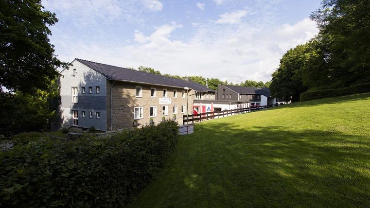 A modern building amidst a green landscape. The sky is blue and the surroundings are calm and inviting.