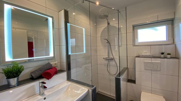 Een moderne badkamer met een glazen douchegebied en een elegant wastafel. Grote spiegels met LED-verlichting en heldere tegels creëren een rustige sfeer.