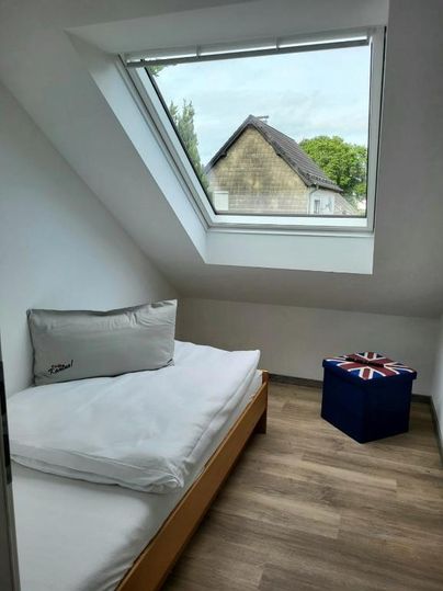 A cozy room with a single bed and a window that lets in daylight. Next to the bed is a seating area with a British motif.