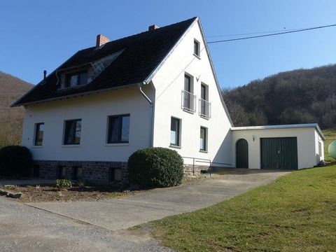 Ein modernes Haus mit weißer Fassade und einem grünen Garagentor. Es liegt in einer ruhigen Umgebung mit sanften Hügeln im Hintergrund.