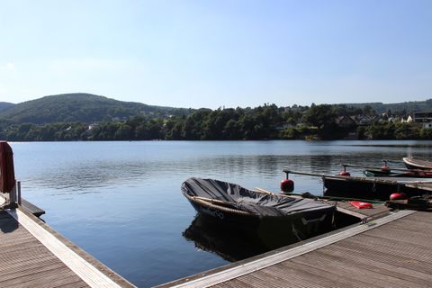 Ein ruhiger See mit einem Boot am Ufer. Im Hintergrund sind sanfte Hügel und ein klarer blauer Himmel zu sehen.
