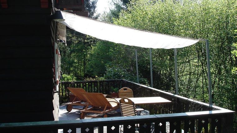 A cozy terrace with loungers and a table. In the background, lush greenery and trees can be seen.