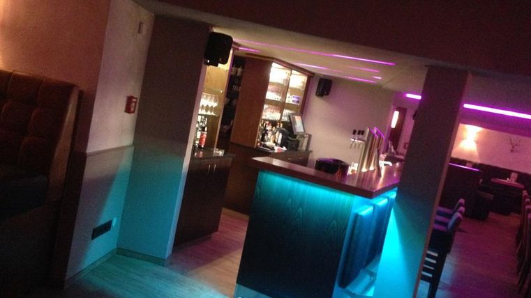 A stylish bar with a illuminated bar counter. The space has cozy seating and soft, colored lighting.