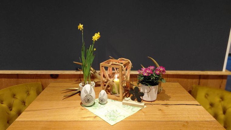 A beautifully decorated table with yellow chairs. On the table are plants, a lantern, and decorative Easter eggs.