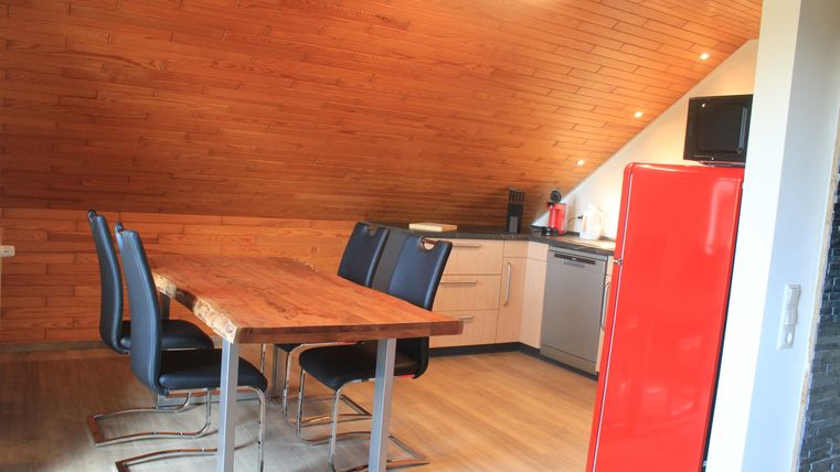 A modern kitchen with wooden cladding and a large dining table. The red refrigerator and the stylish chairs make a striking accent.
