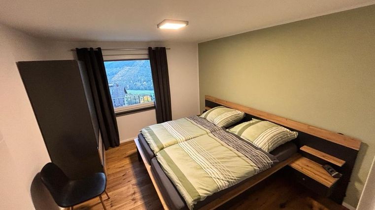 A modern bedroom with a large double bed and a cozy sitting area. The window offers a view of the landscape.