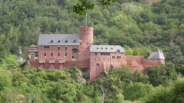 Een indrukwekkend kasteel temidden van groene heuvels. De karakteristieke rode bakstenen muren en de markante toren bepalen het landschap.