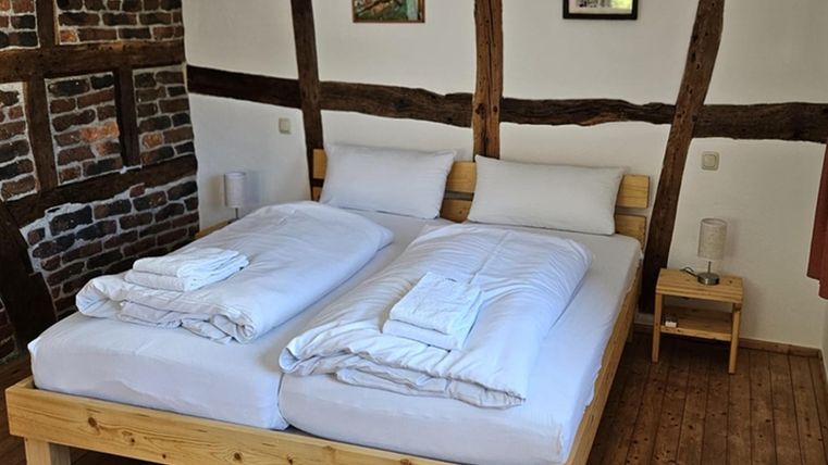 A cozy bedroom with a double bed and fresh bed linens. The walls are partly half-timbered, and the decor is simple and modern.