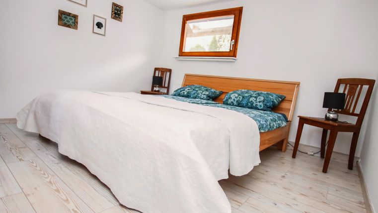 Een lichte slaapkamer met een tweepersoonsbed en gezellige kussens. Naast het bed staat een houten stoel en een nachttafeltje met een lamp.