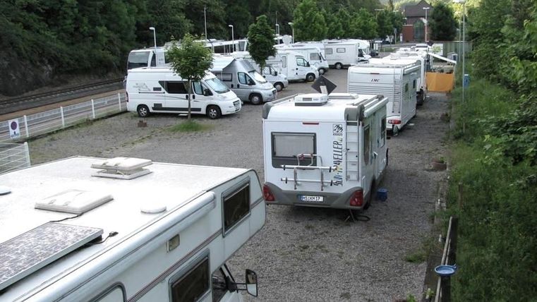 Ein Stellplatz für Wohnmobile mit mehreren Fahrzeugen. Umgeben von Bäumen und sanften Hügeln.