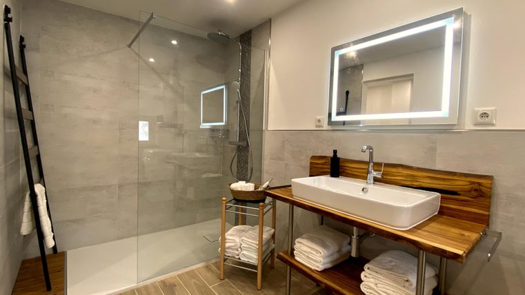 Een moderne badkamer met een ruime, glazen douche en een elegant wastafel. Houten planken met frisse handdoeken maken het geheel compleet.