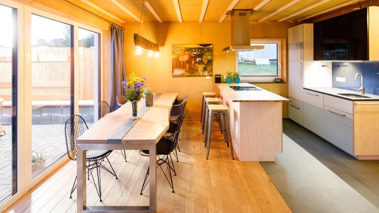 A modern kitchen with a large dining table and stylish chairs. The bright light creates an inviting atmosphere.