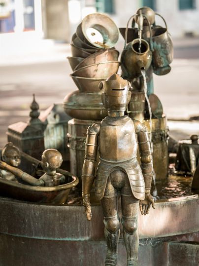 A sculptural fountain installation featuring a metal figure and various vessels. The fountain is artistically designed and conveys a creative atmosphere.