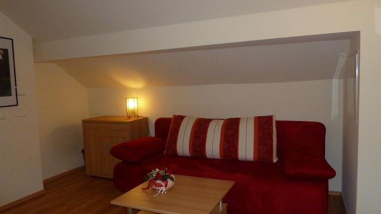 A cozy living room with a red sofa and a small wooden table. The walls are light, and there is a lamp that illuminates the room pleasantly.