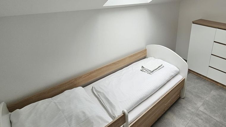 Een eenvoudig kamer met een eenpersoonsbed en een kast. Het heeft een lichte, moderne uitstraling en een dakraam.