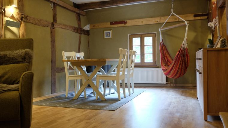 Een gezellige woonkamer met een tafel en stoelen, evenals een hangstoel. De muren zijn in een warme tint geschilderd en houten details geven de ruimte een rustieke uitstraling.