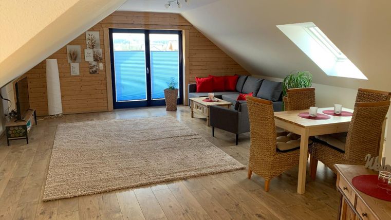 A bright, modern living room in the attic with a cozy sofa, a table, and chairs. Large windows provide plenty of daylight and a view outside.