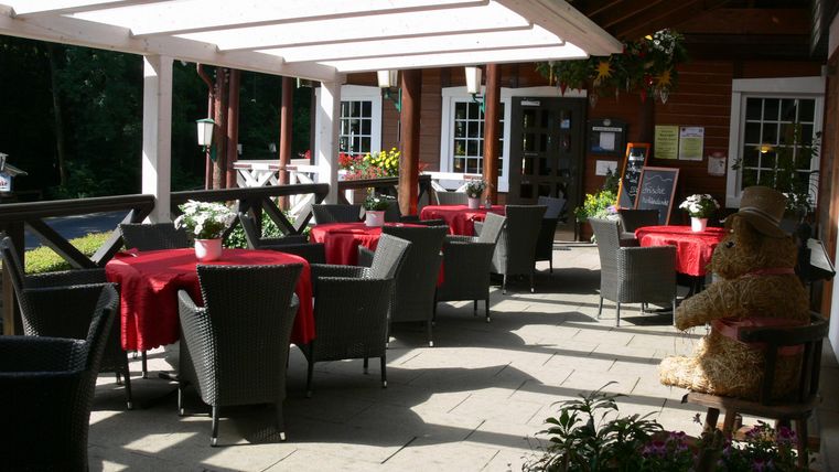 A cozy terrace with tables and chairs, adorned with red tablecloths. In the background, there is a decorative straw figure.