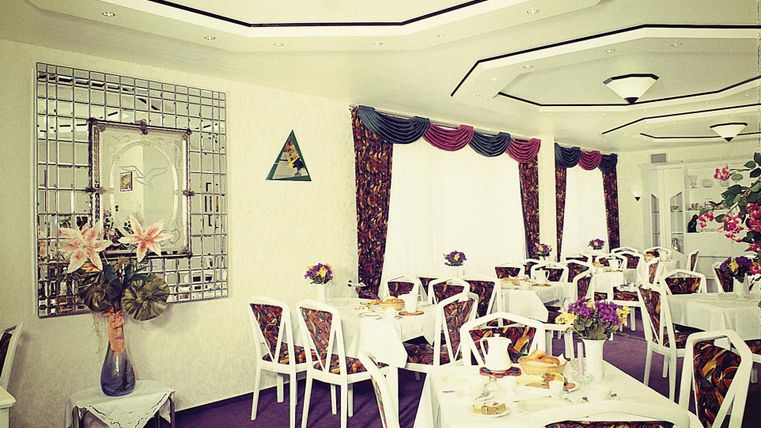 Een elegan restaurant met witte tafels en kleurrijke stoelen. De muren zijn smaakvol gedecoreerd, en er zijn mooie bloemstukken op de tafels.
