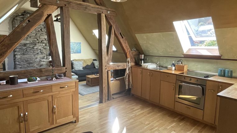 Een gezellige keuken met houten meubels en modern design. Op de achtergrond is een woonruimte met een comfortabele bank te zien.