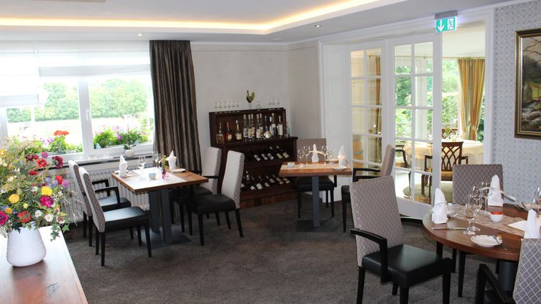 An elegant restaurant with stylishly set tables. Large windows let in plenty of daylight and offer a view of the outside.
