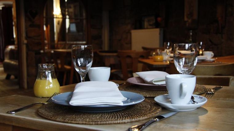 A laid table with plates, glasses, and cutlery in a cozy restaurant. In the background, additional seating and a relaxed atmosphere can be seen.
