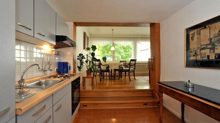 Een moderne keuken met grijze kasten en een spoelgedeelte. Op de achtergrond is een eetgedeelte met een tafel en stoelen te zien.
