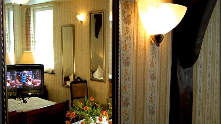 Ein gemütlicher Raum mit hellem Licht und dekorativen Wänden. Im Hintergrund steht ein Fernseher und ein Tisch mit frischen Blumen.