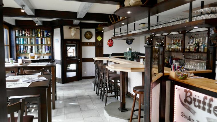 A cozy restaurant with a wooden bar and modern furniture. The walls are decorated and the space is bright and inviting.