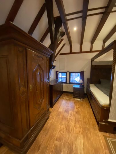 Een gezellige slaapkamer met houten vloeren en zichtbare plafondbalken. Er is een grote kast en een bed in een rustieke stijl.