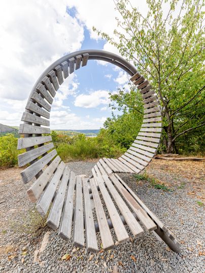 Een creatieve houten bank in de vorm van een cirkel. Op de achtergrond ziet men een groene heuvel en de blauwe lucht.
