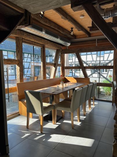 A modern restaurant with a large table and elegant chairs. Large windows provide plenty of natural light and a view outside.