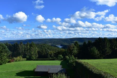 A picturesque landscape with green meadows and trees. The sky is blue, and white clouds are floating above.