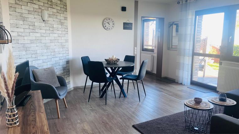 A bright and modern living room with a dining table and chairs. Large windows provide plenty of daylight and a welcoming atmosphere.