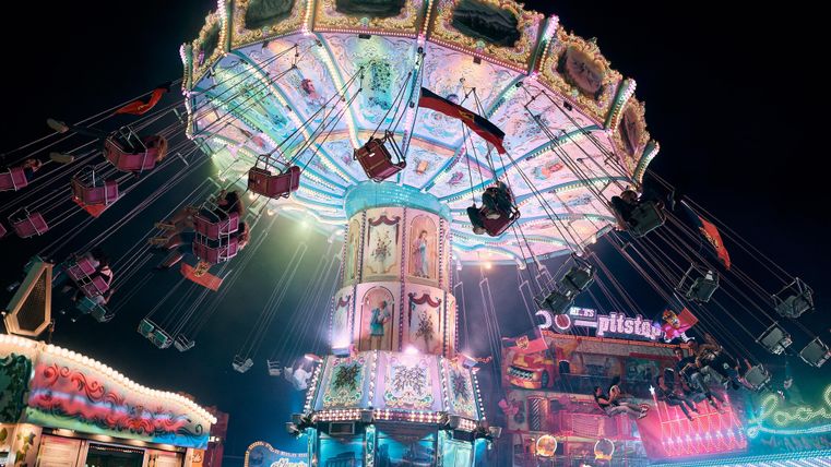 Ein bunter Karussell mit leuchtenden Lichtern auf einem Jahrmarkt bei Nacht. Die Schaukeln sind hoch oben und bieten eine fröhliche Atmosphäre.